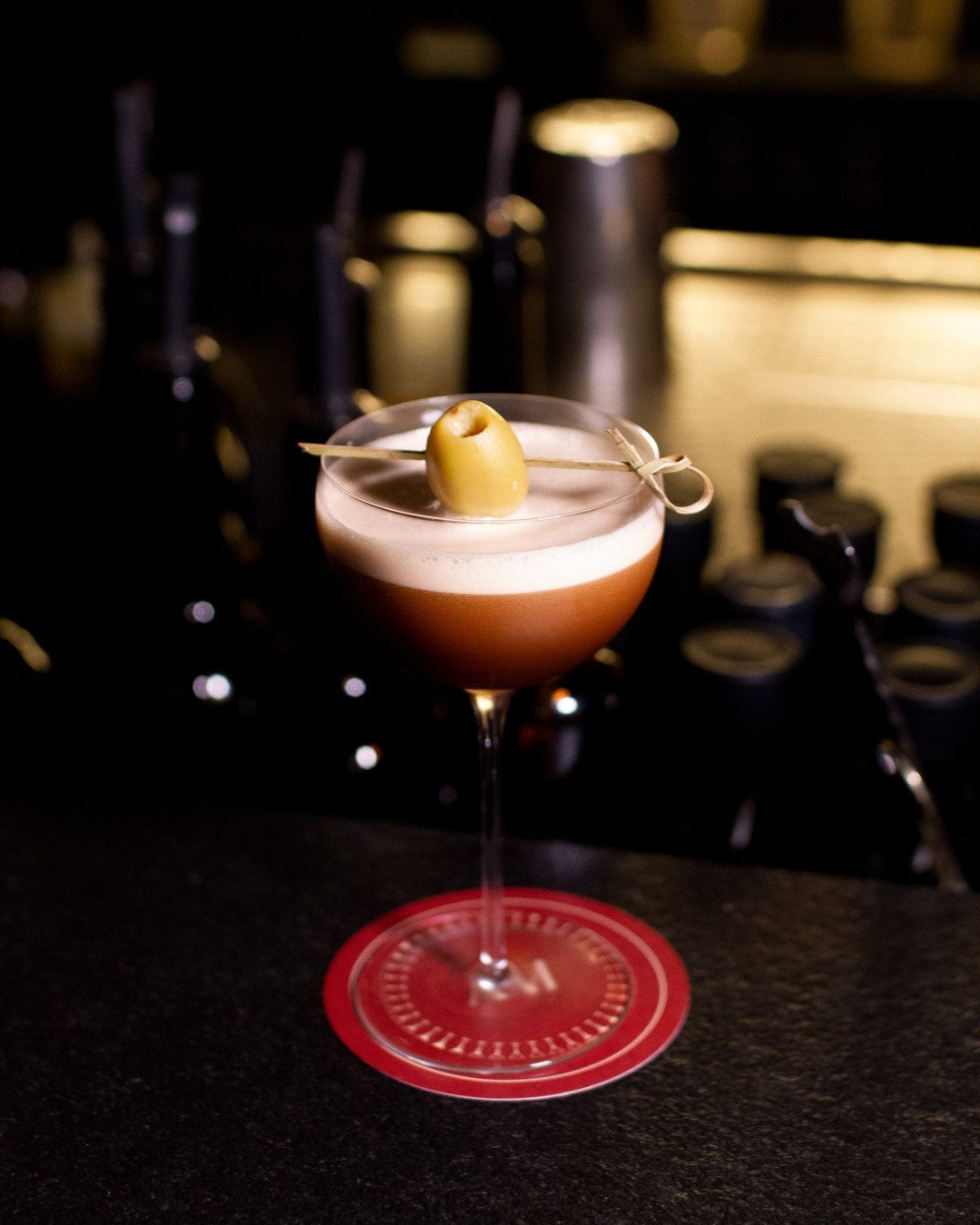 Olive Oil Espresso Martini in a coupe with a foamy top and a single olive on a pick
