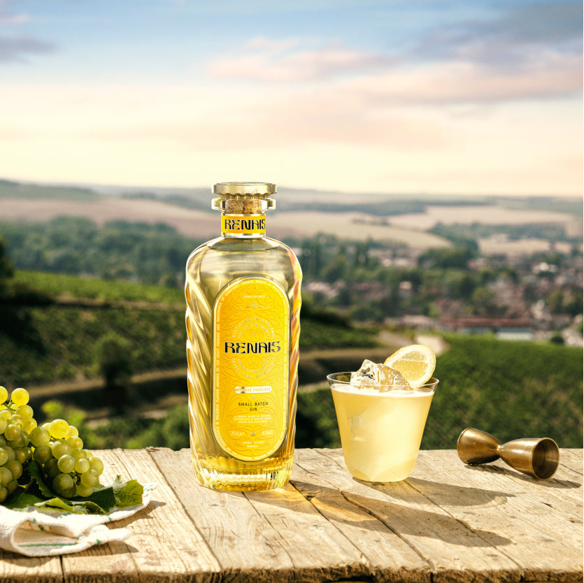 Renais bottle next to a cocktail and bunch of grapes with vineyard in background